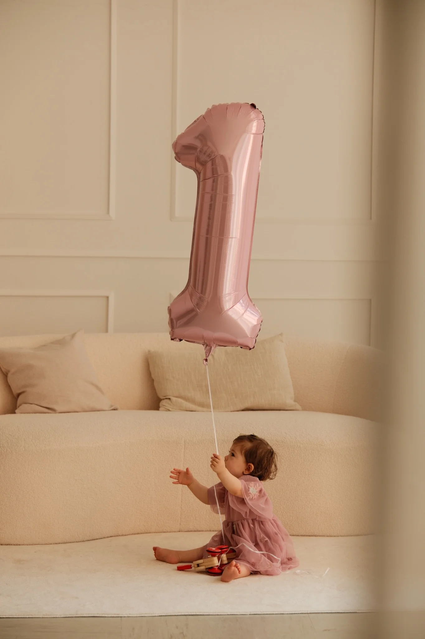 Kind sitzt mit einem Ballon zur Eins vor dem Sofa